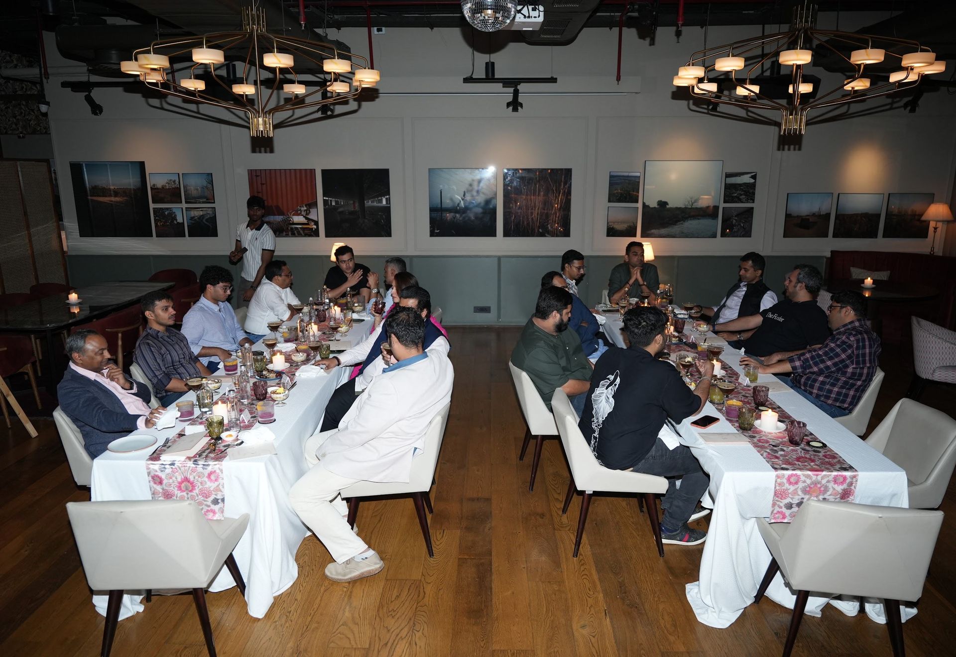 A long dinner table of founders mid-conversation under warm light.